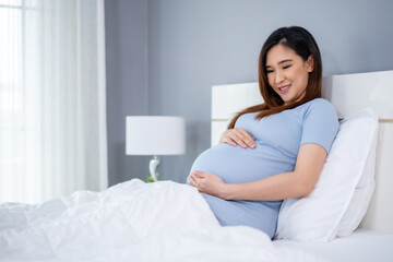 Obraz na płótnie Canvas happy pregnant woman stroking her belly on bed