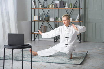 Woman practice Tai Chi Chuan  and conducts online training on the laptop  in a home. Social Distancing.  webinar recording. online communication. 
