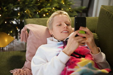 a woman uses a mobile phone lying on the couch at home. ordering Christmas gifts online.  chat with friends online on Christmas night