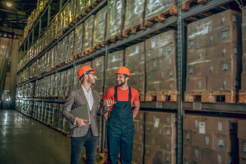 Naklejka na ściany i meble Manager in orange helmet talking to the worker while inspecting the warehouse