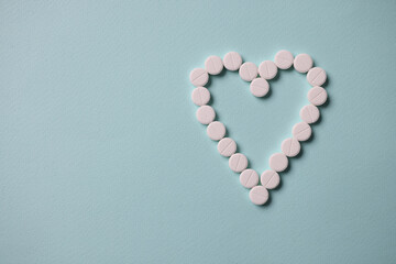 White tablets lying in shape of heart on blue background. Heart disease treatment concept