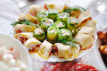 On the festive table is a plate with a delicious snack. Pancake rolls with fish and cucumber vegetable rolls.