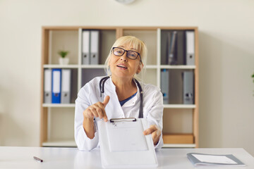 Doctor sits in front of the camera and shows a prescription to her patient using a video call.