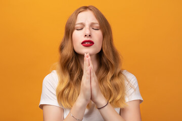 Pretty girl with wavy redhead, holding palms together, praying for peace and love, having peaceful facial expression