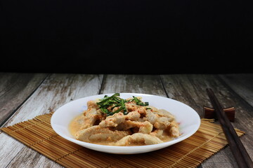 Boiled chicken thigh with red curry and fresh coconut milk topping with Kaffir lime leaves on the plate. Famous traditional appetizer menu in Asian restaurant. 