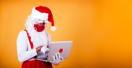 modern Santa Claus wearing a red protective face mask checking orders on a laptop. Santa Claus using technology in pandemic time concept