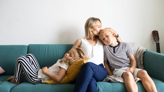 Blonde mom kissing her son&rsquo;s head and relaxing with daughter on the couch blank space