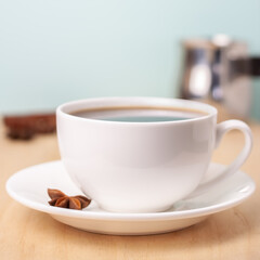 White ceramic cup of coffee on plate with half star anise, cinnamon sticks and turka behind blue background