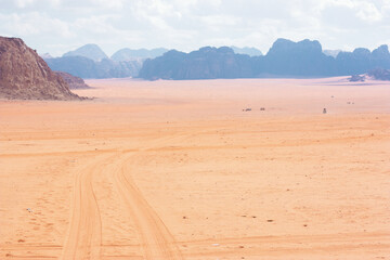 Wadi Ram desert in Jordan, mountains on the horizon in a blue haze, car tracks on the sand