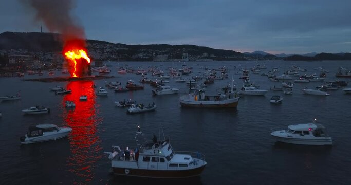 Unbelievably beautiful, cinematic, approaching aerial footage that reveals the biggest bonfire event on Earth and the small boats that are gathering around it near Alesund, Norway at dusk.