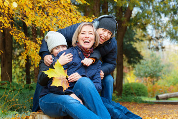 Fototapeta premium portrait of a mother and son and daughter in autumn city park, happy people together, parent and children talking and smiling, sitting on a stump, beautiful nature
