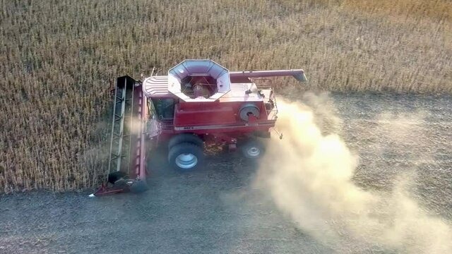 Aerial pan view of red combine harvesting beans in farmers field near sundown in the Midwest USA
