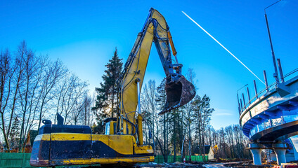 raised excavator bucket against the sky with a flying plane