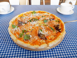 Fresh round pizza with red fish greens and cheese stands on the table with a checkered tablecloth and two white cups