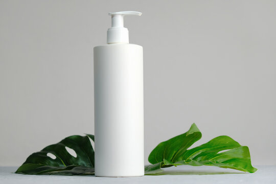 Blank plastic cosmetics container for cream or shampoo. Cosmetics bottle mockup with tropical leaves. Beauty product design, skincare and haircare concept.