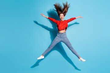 Full length photo of crazy lady jump up spread arms legs hair flying wear red sweater sneakers jeans isolated blue color background