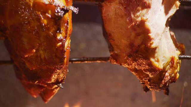 Extreme close-up delicious pork knuckles rotates on special support over burning fire preparing at bright electric light against dark street extreme closeup. Easter fair in Prague