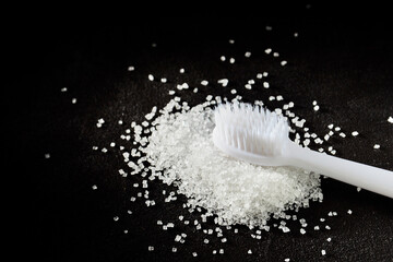 new white toothbrush and a handful of sprinkled sugar on a dark background. dental treatment and caries concept