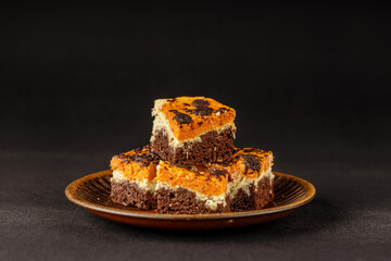 Delicious pumpkin cake with cheese cream and cacao or chocolate on the top on the black background with copy space