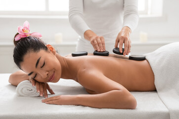Obraz na płótnie Canvas Relaxed asian woman enjoying hot stones back massage in spa salon