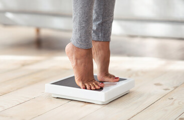 Cropped view of young black woman standing on scales at home, measuring her weight, closeup of feet