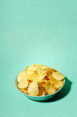 Vertical image.Blue bowl full of salty potatoes chips on the blue background.Empty space
