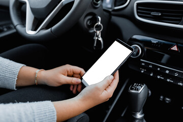 Obraz premium Young driver using smartphon in the car while driving or parking. Mockup of a mobile phone with isolated white screen in the hands of a woman.