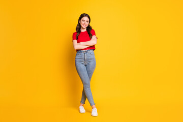 Full size photo of charming lady hold arms crossed wear casual red t-shirt cropped top jeans shoes isolated yellow color background