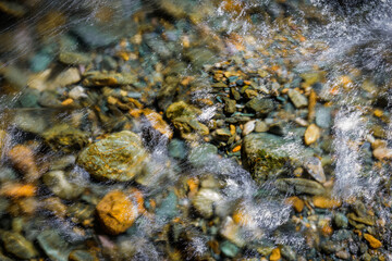 Rocky bottom of mountain river through the clear water, selective focus, blurring the image. Cristal water in the stream shimmers in sunlight. Stone background.