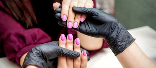 Hands of manicurist holds female fingernails with pink nail polish in nail salon