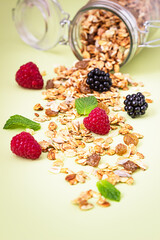 Composition with muesli or granola in jar with raspberries, blackberries and mint on pastel green background. Healthy food concept.