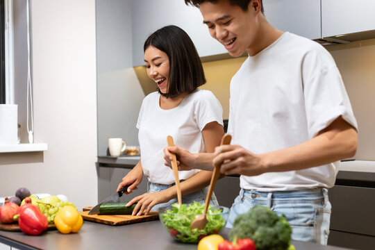 Asian Couple Cooks In Modern Kitchen, Laughing During Dinner Preparartion