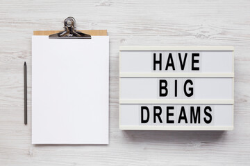 'Have Big Dreams' on a lightbox, clipboard with blank sheet of paper on a white wooden surface, top view. Flat lay, overhead, from above.