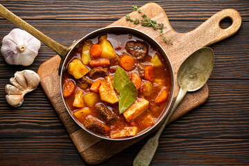 Delicious stew with meat, potatoes, carrot and gravy in old rustic copper pot on brown wooden...