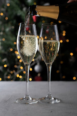 Sparkling wine is poured into glasses against the background of a Christmas tree. Bokeh. Christmas together. Vertical