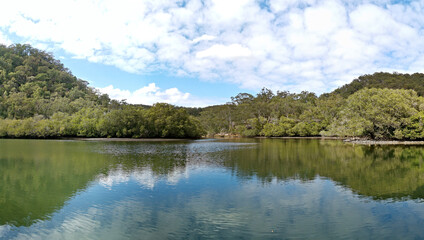 Beautiful morning view of a creek with reflections of deep blue sky, light clouds, mountains and trees, Cockle Creek, Bobbin Head, Ku-ring-gai Chase National Park, New South Wales, Australia
