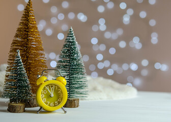 Yellow alarm clock and a Christmas tree on the table.