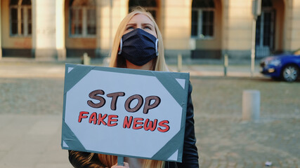 Young woman in protective mask protesting against fake news. She walking down the street with...