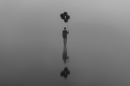 surreal creative portrait of a man in a suit with a hat with balloons in his hand on the water