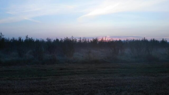 Dutch foggy morning hanging between the grass on the ground. When the drone lifts the pedestal shot a pretty sunrise behinds buildings on the background become visual.