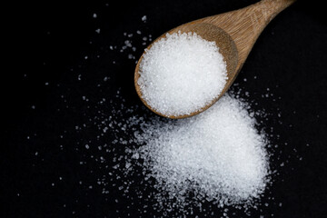 Pile white sugar in wooden spoon on black background and copy space
