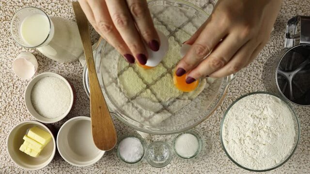 Woman hands prepares liquid dough. Break raw eggs into a glass bowl. Top view, close up.
