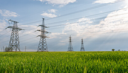 High voltage lines and power pylons and a green agricultural landscape on a sunny day.