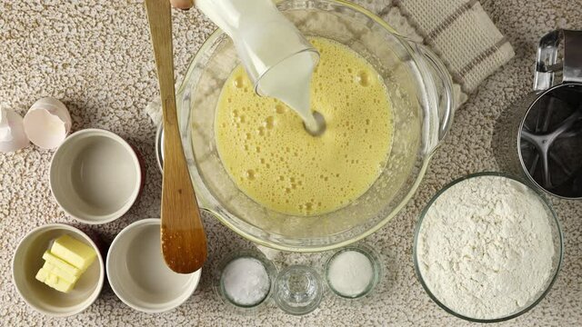 Woman hands prepares liquid dough for baking. Adding milk in glass bowl.  Top view, close up.