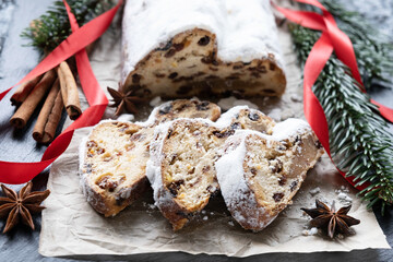 christmas cake with marzipan, nuts and raisins on parchment paper, cinnamon and anise, spruce branches with red ribbons