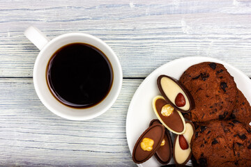 Chocolates, a cup of coffee and cookies with chocolate chips on a light wooden table. View from above.