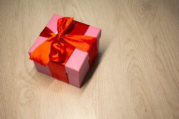 pink Christmas gift box tied with a red ribbon and tied with a bow. on a light gray laminate. horizontal. close up. Christmas. New Year. Minimalistic. love. indoor. holiday symbol. decoration.