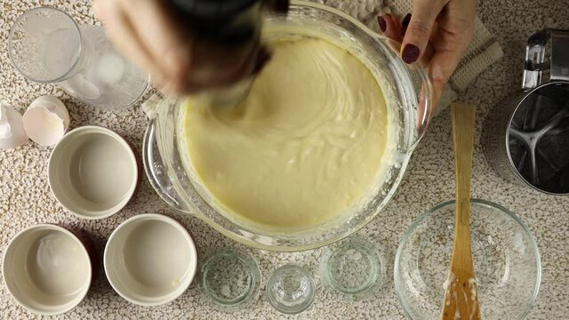 Process of making and whisking the dough, woman's hand mixing liquid dough with electronic mixer whisk in glass bowl.