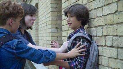 Side view of aggressive boys pushing scared victim to wall on schoolyard. Rude Caucasian classmates bullying schoolboy outdoors. Lifestyle and physical abuse.