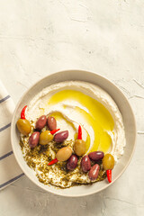 Popular middle eastern appetizer labneh or labaneh, soft white goat milk cheese with olive oil, hyssop or zaatar, olives on grey table, top view ,flat lay. Close up image.